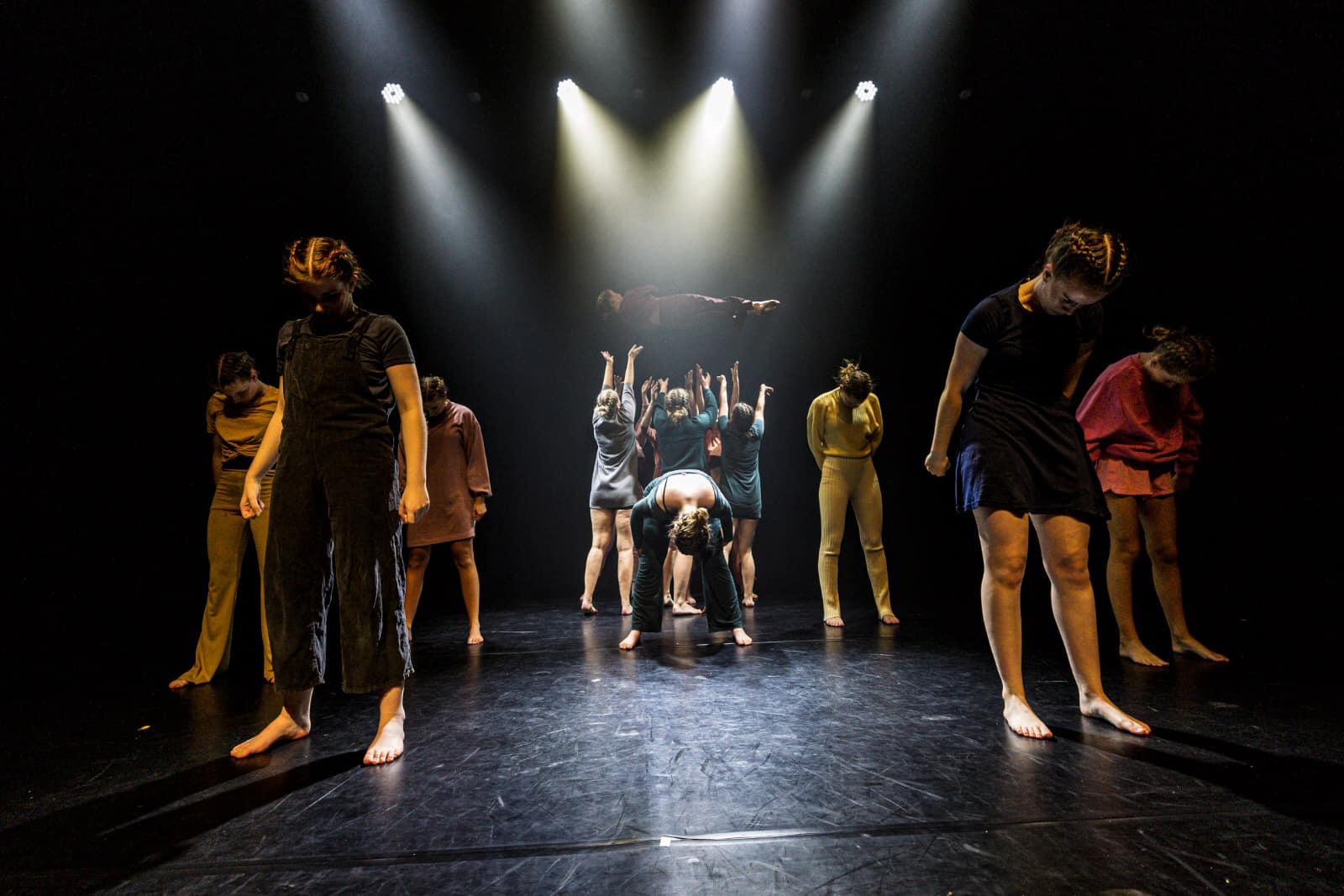 scenebeeld van een dansvoorstelling. We zien een jonge vrouw op een wipwap staan, uitgelicht met 4 spots